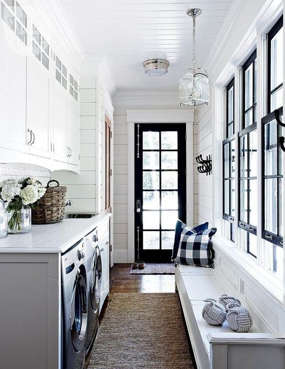 a black and white mudroom laundry with a white bench and plaid pillows, white cabinets, a washing machine and a dryer and black framed windows