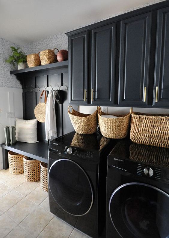 a black mudroom entry with shaker cabinets, an open storage unit with baskets, potted plants and a washing machine and a dryer