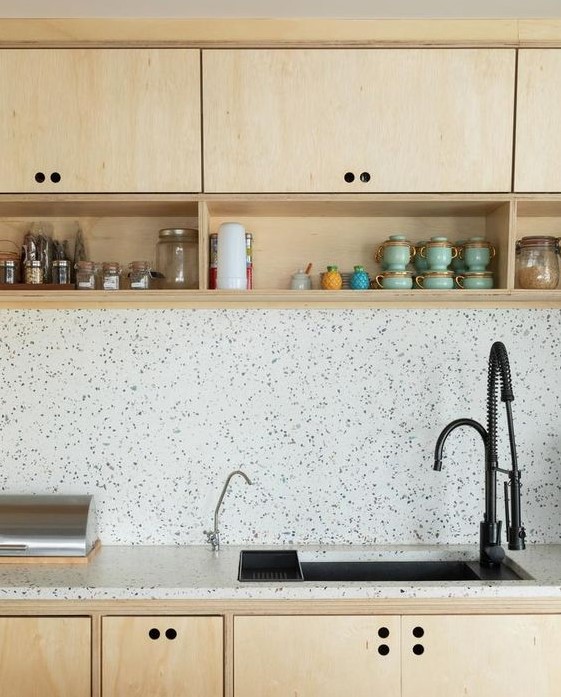 a blonde wood kitchen with black fixtures and a black and white terrazzo countertop and a backsplash for a refreshing and cool look