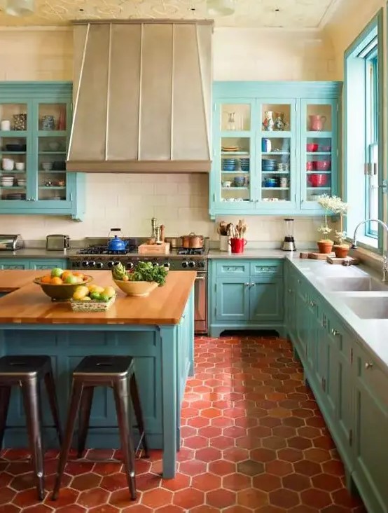 a bright blue kitchen with terracotta tile on the floor, a large vintage hood, butcher block countertops and a patterned ceiling