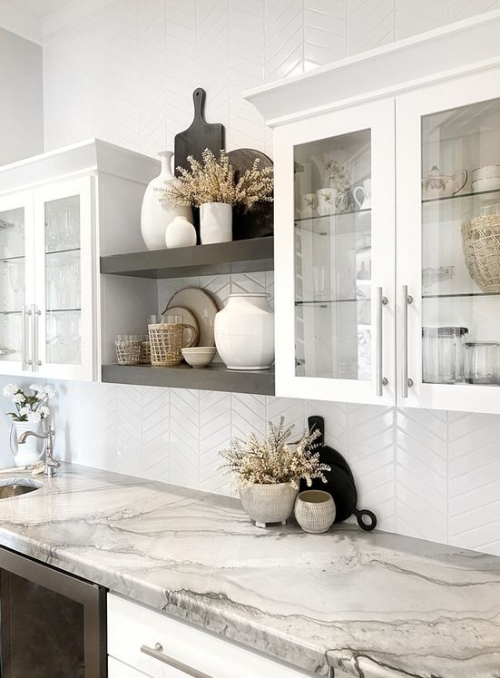 a catchy kitchen with white flat panel and glass cabinets, black built-in shelves and built-in appliances, a white chevron backsplash