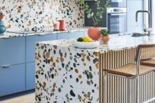 a cheerful kitchen with blue sleek cabinets and bright terrazzo countertops and a backsplash plus coral pendant lamps
