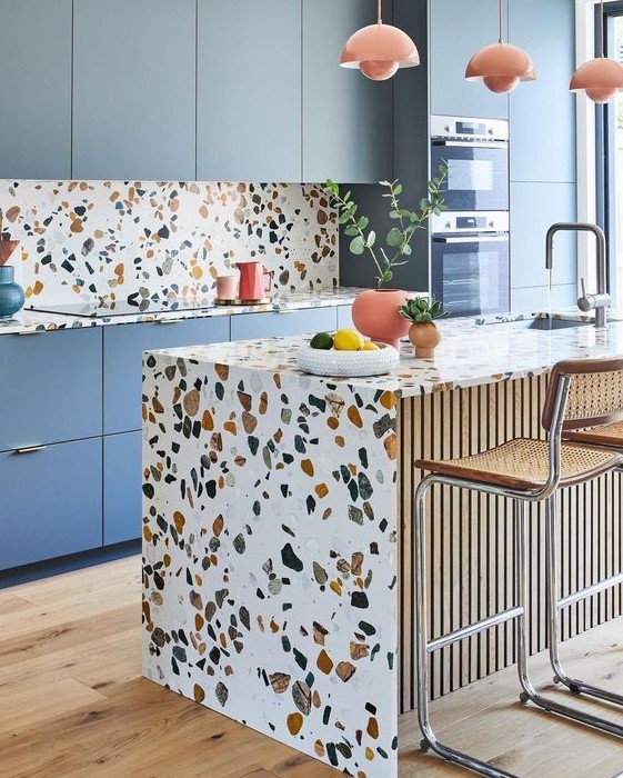a cheerful kitchen with blue sleek cabinets and bright terrazzo countertops and a backsplash plus coral pendant lamps
