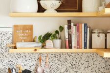 a chic kitchen with a black and white terrazzo countertop and backsplash plus open blonde wood shelves looks fresh and more modern