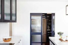 a chic modern kitchen with white flat panel and reeded glass cabinets, navy frame fluted glass doors and white stone countertops