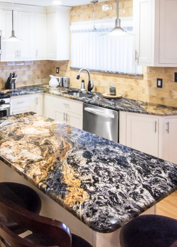 a chic modern white kitchen with shaker cabinets, a beige tile backsplash, black, white and gold granite countertops