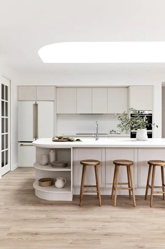 a chic neutral kitchen with shaker style cabinets, a curved kitchen island with open storage compartments and a skylight over it
