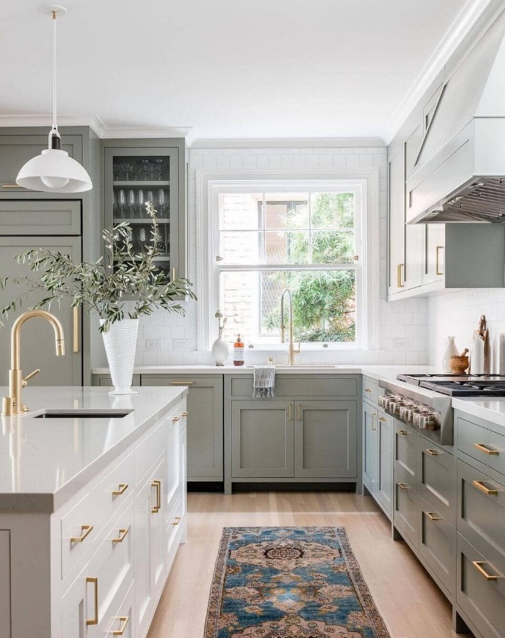 a classic sage green kitchen with shaker and glass front cabinets, a white stone countertop and square tiles, a creamy kitchen island