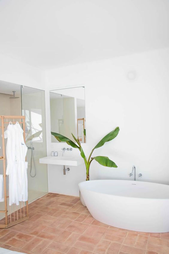 a contemporary bathroom in neutrals, with a terracotta tile floor, an oval tub, a glass-enclosed shower space, a wall-mounted sink