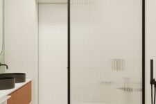 a contemporary bathroom with a bright terrazzo floor, a floating vanity with black sinks, a shower space with a ribbed glass space divider