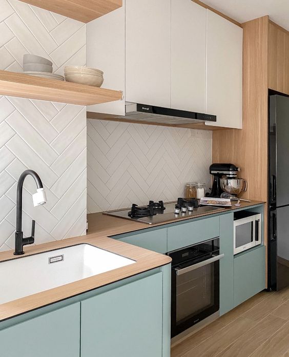 a contemporary kitchen with sage green and white flat panel cabinets, wooden countertops, a white herringbone tile backsplash