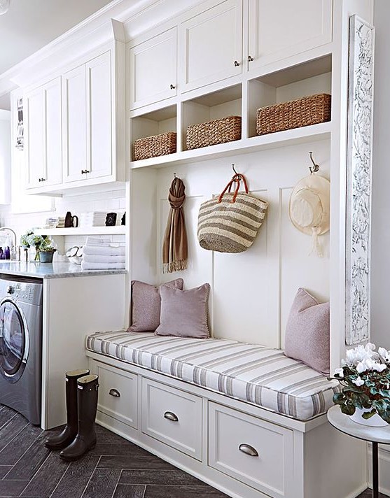 a cozy creamy farmhouse laundry mudroom with shaker cabinets and an open storage unit with an upholstered bench and appliances