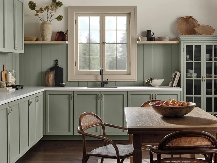 a cozy sage green kitchen with shaker cabinets, white stone countertops, a dining zone with stained furniture
