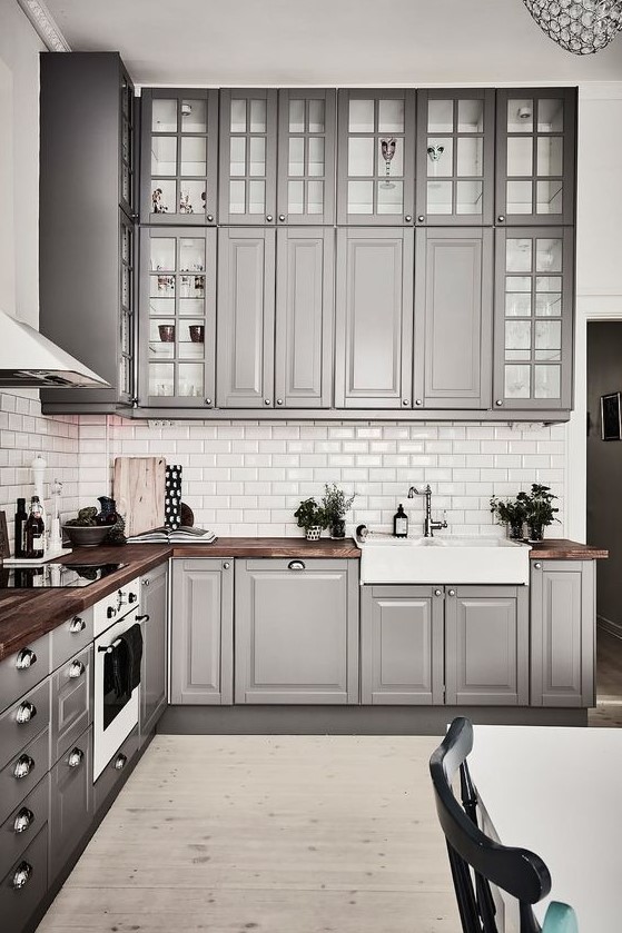 a cozy traditional grey kitchen with usual and glass cabinets, with rich-colored wooden countertops and metal knobs