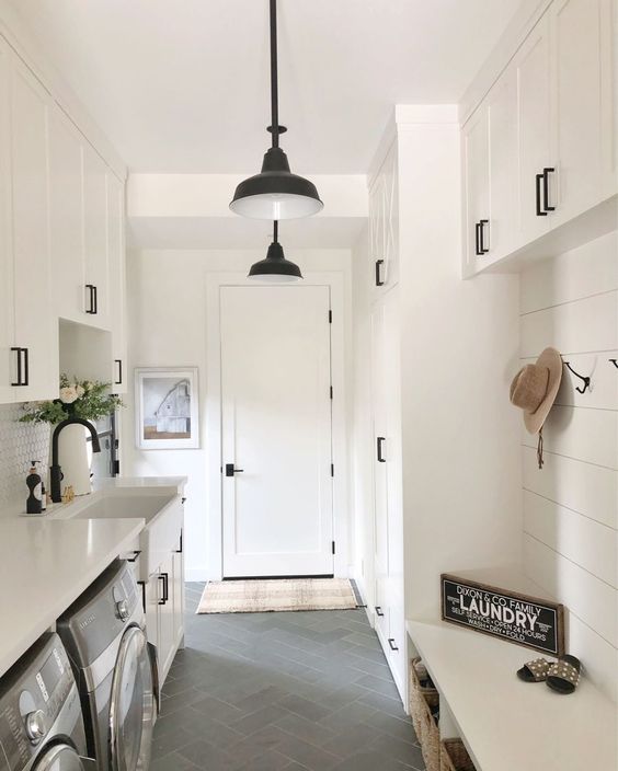 a creamy farmhouse mudroom laundry with a slatted wall, shaker style cabinets, a washing machine and a dryer and black fixtures