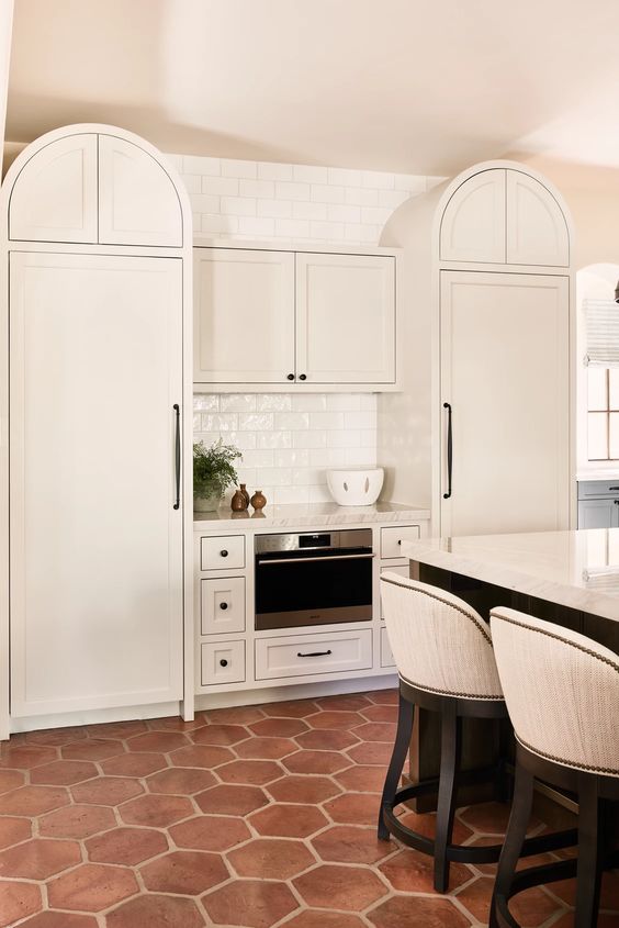a creamy kitchen with curved cabinets, a large kitchen island with a seating zone and a terracotta tile floor that adds interest and texture