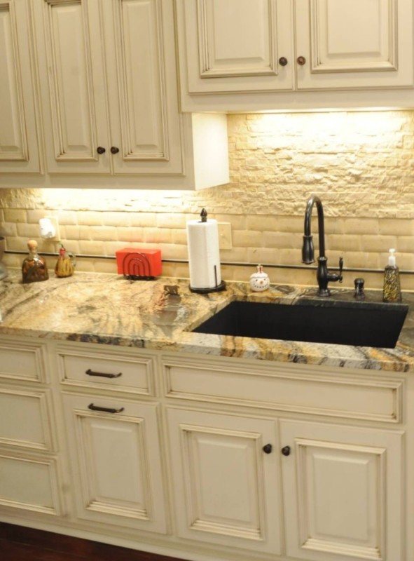 a creamy kitchen with shaker cabinets, a white tile and faux stone backsplash, built-in lights and a gold granite countertop that makes a statement