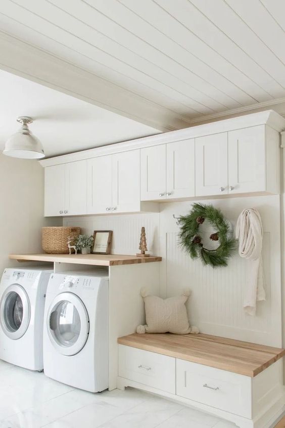 a creamy mudroom laundry with shaker cabinets, an open rack with a storage bench and a washing machine and a dryer