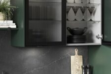 a dark green kitchen with shaker cabients and black fluted glass cabinets, a black marble backsplash and countertops is a chic and refined space