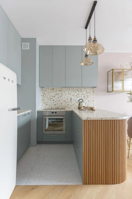 a delicate kitchen with grey blue flat panel cabinets, a fluted kitchen island, terrazzo countertops and a backsplash