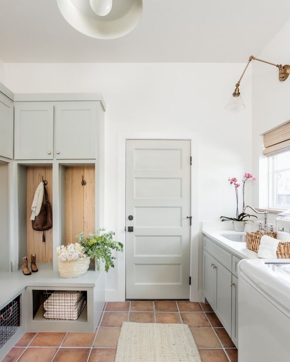 a dove grey laundry mudroom with shaker cabinets, an open rack with cabients, a washing machine and a dryer and brass sconces