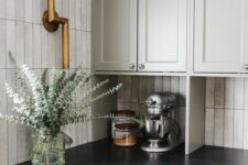a dove grey shaker style kitchen with a skinny tile backsplash, black soapstone countertops and brass fixtures