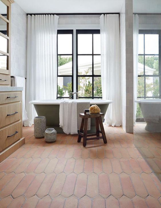 a farmhouse bathroom with a glazed wall, a green bathtub, a stained vanity, a terracotta tile floor and a glass-enclosed shower