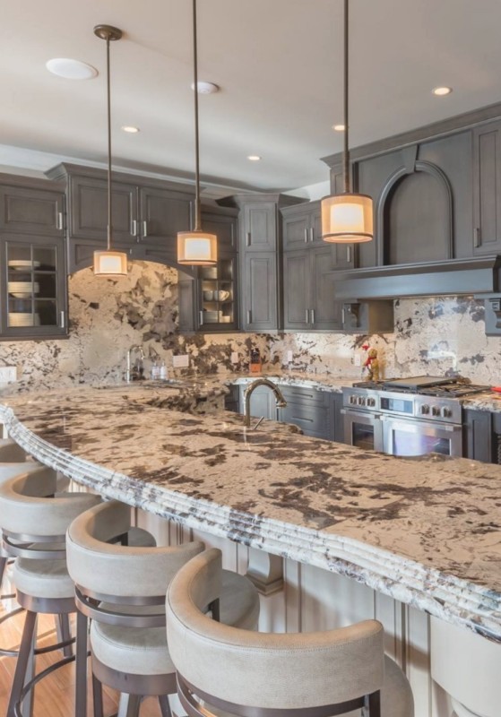 a farmhouse kitchen with vintage flare, with grey shaker style cabinets, grey and white countertops, pendant lamps and creamy chairs