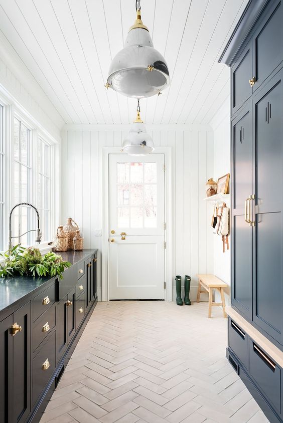 a farmhouse mudroom laundry with navy shaker cabinets, black countertops, a stained bench and glossy pendant lamps