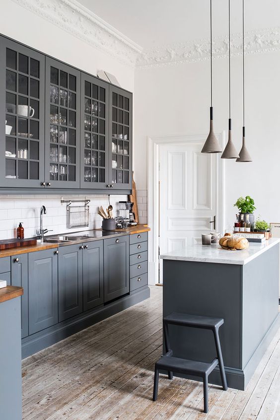 a graphite grey kitchen with shaker and glass cabinets, a white subway tile backsplash, butcherblock countertops and pendant lamps