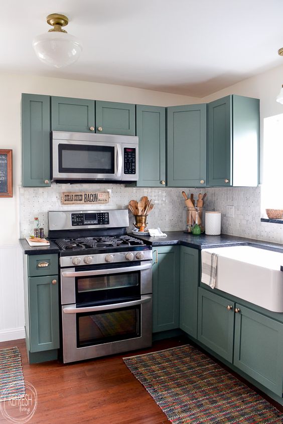 a green kitchen with shaker cabinets, black soapstone countertops and a neutral glossy tile backsplash plus stainless steel fixtures