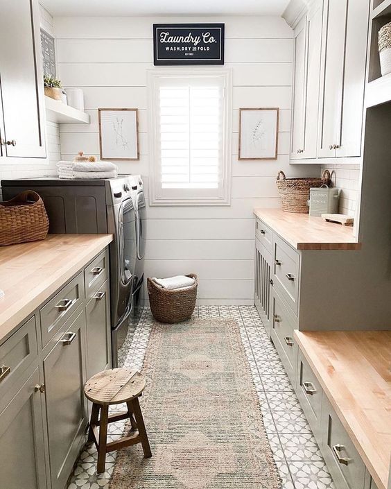 a grey and white mudroom laundry with shaker cabinets, butcherblock countertops, a beadboard wall and a printed rug