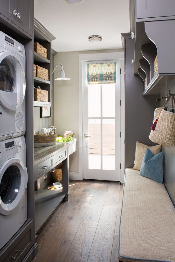 a grey farmhouse mudroom laundry with shaker cabinets and an open storage unit, an upholstered bench, a washing machine and a dryer