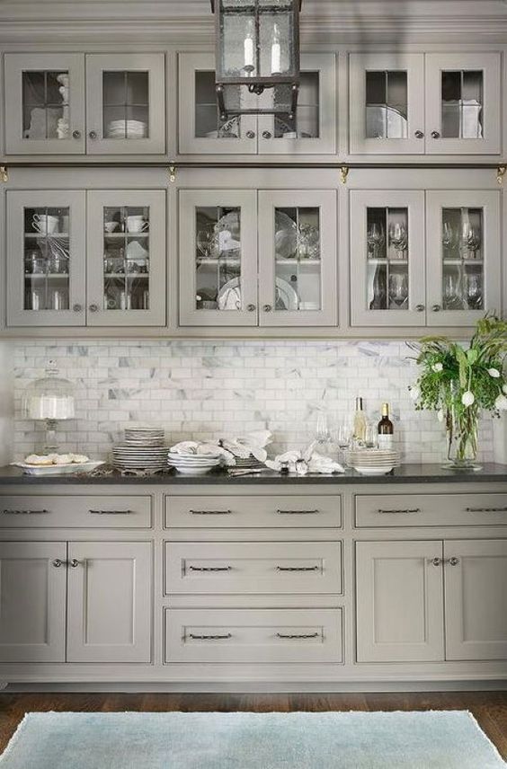 a grey kitchen with shaker and glass front cabinets, a white marble tile backsplash and black countertops