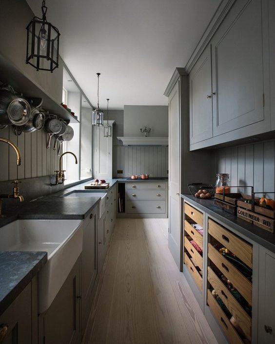 a grey kitchen with shaker panel and shaker cabinets, black soapstone countertops, brass fixtures and beadboard backsplashes
