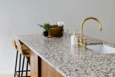 a kitchen island with rather a neutral yet stylish countertop, a gold faucet and some rattan stools is very elegant and chic