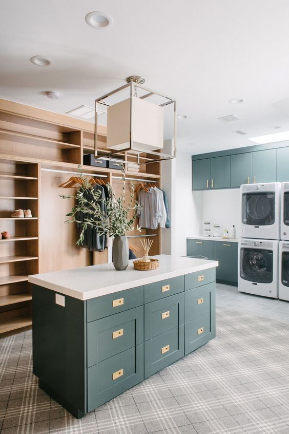 a large modern laundry mudroom with dark green cabinets, white countertops, a light-stained storage unit, a chandelier and washing machines and dryers