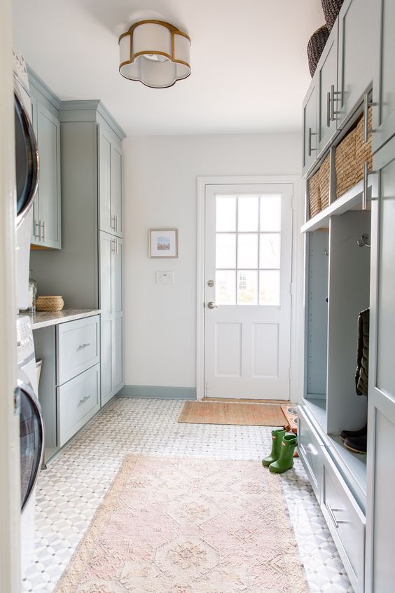 a light blue mudroom laundry with shaker cabinets, an open storage unit, baskets and printed rugs, a washing machine and a dryer