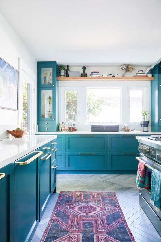 a lovely bright blue kitchen with shaker and glass front cabinets, white countertops, gold handles and a bold printed rug is wow