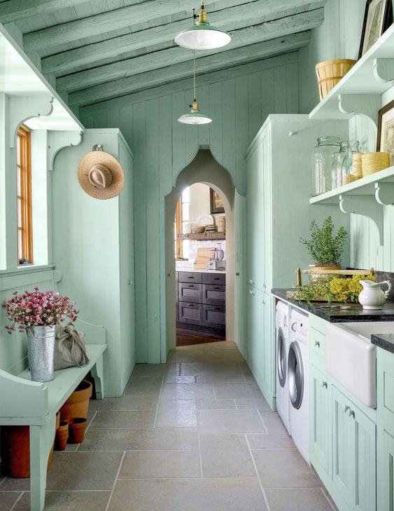 a lovely mint green mudroom laundry with shaker cabinets, open shelves and a matching bench, a washing machine and a dryer and pendant lamps
