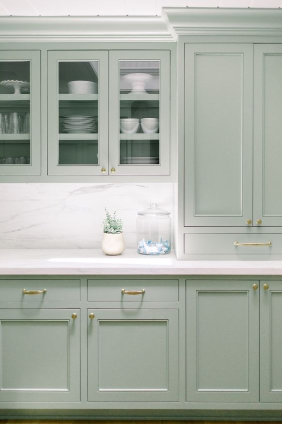 a lovely mint kitchen with shaker and glass front cabinets, a white marble backsplash and countertops and gold handles