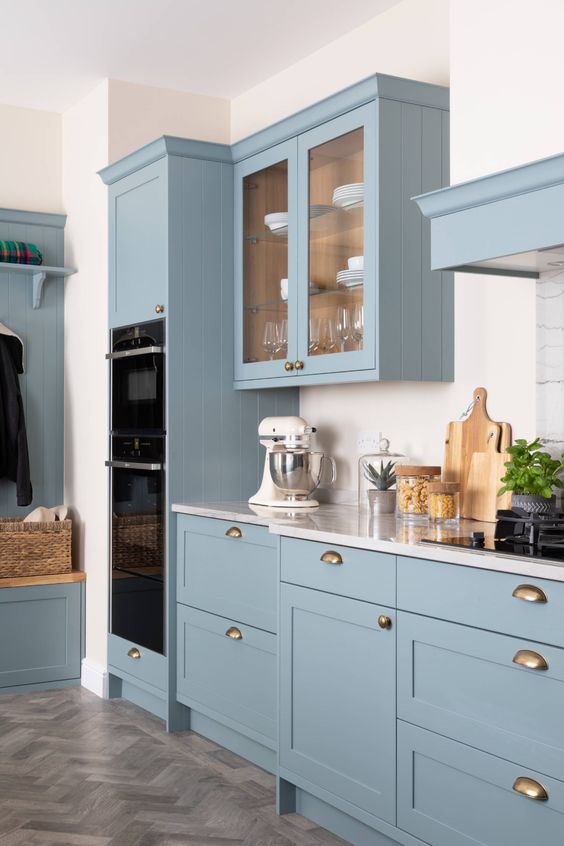 a lovely skinny shaker and glass front kitchen with white stone countertops and a white backsplash plus brass touches