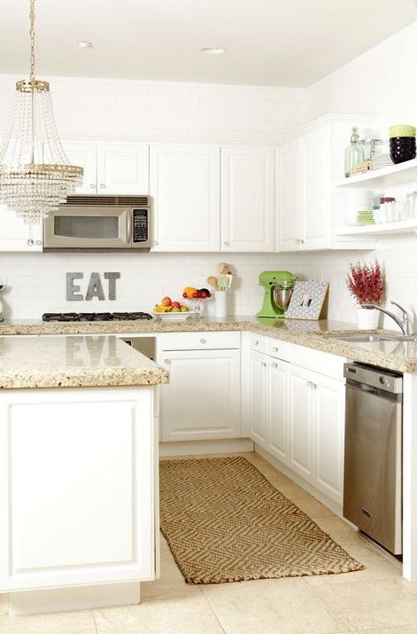 a lovely white kitchen with grey granite countertops, a white tile backsplash and a refined crystal chandelier
