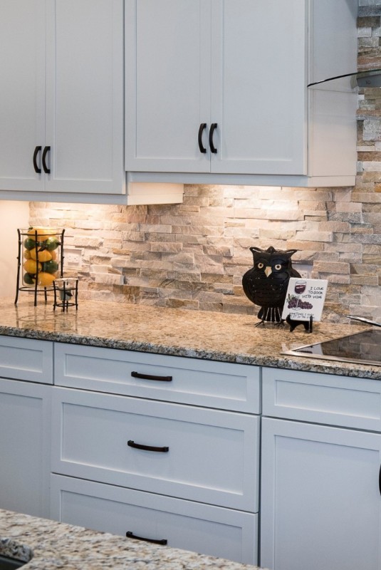 a lovely white kitchen with shaker cabinets, a faux stone backsplash and grey granite countertops is a chic space