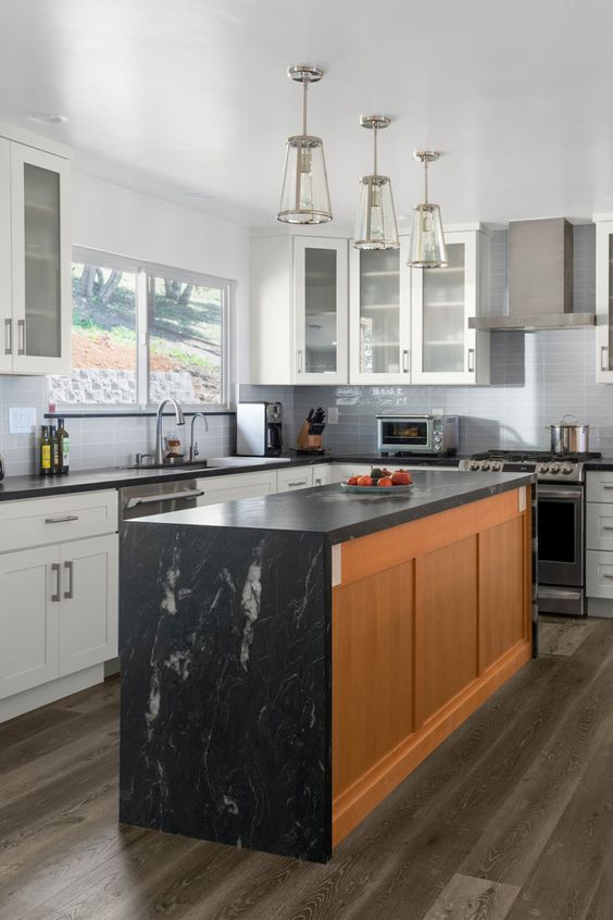 a lovely white kitchen with shaker cabinets, a stained kitchen island, black soapstone countertops and hanging lamps