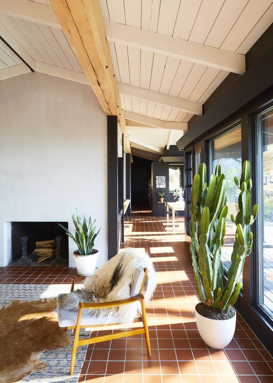 a mid-century modern living room with glazed walls, a terracotta tile floor, a fireplace, some seating furniture, potted plants