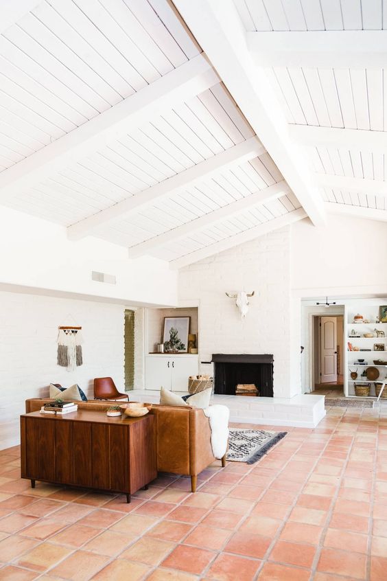 a mid-century modern living room with white walls and a ceiling, a terracotta tile floor, a leather sofa, a stained cabinet and a fireplace