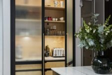 a mini built-in pantry with fluted glass black frame cabinets, black and gold pendant bulbs and a brass kitchen island