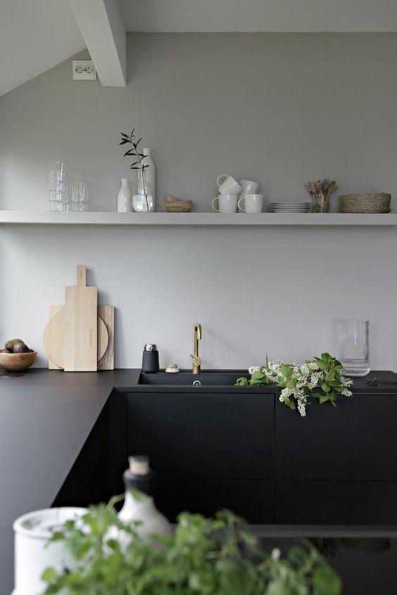 a minimalist kitchen with flat panel lower cabinets and black soapstone countertops, grey walls and a matching grey shelf