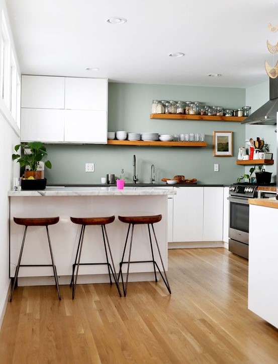 a minimalist kitchen with white cabinets, sage green walls, stone countertops and wooden shelves and stools